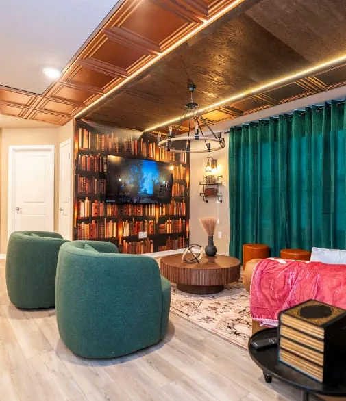 Sala temática aconchegante com detalhes em madeira, papel de parede de biblioteca, poltronas verdes e iluminação decorativa.